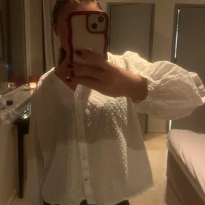 Vit blus med knappar - Säljer en stilren vit blus med knappar framtill. Blusen har långa ärmar med volangdetaljer och en v-ringad hals. Perfekt för en chic och elegant look.