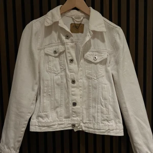 Vit jeansjacka  - Snygg vit jeansjacka med klassisk krage och knappar framtill. Jackan har två bröstfickor med lock och knapp samt långa ärmar. Perfekt för en stilren look.