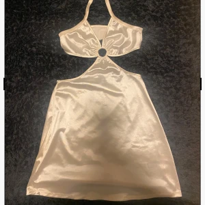 vit/ Champagnefärgad klänning från Divided - Snygg vit klänning från Divided H&M med halterneck och en ringdetalj framtill. Klänningen har en glansig finish och är perfekt för festliga tillfällen.