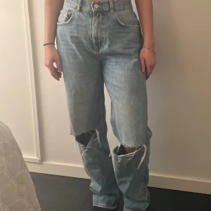 Blå jeans med slitningar från gina tricot - Säljer ett par blå jeans från gina tricot med coola slitningar på knäna. De har en hög midja och en straight passform som ger en avslappnad look. Perfekta för en trendig stil!