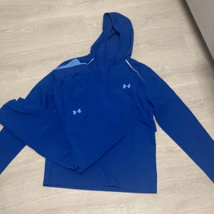 Blå hoodie och byxor från Under Armour - Snygg blå hoodie och matchande byxor från Under Armour. Hoodien har en justerbar huva och långa ärmar med logga på bröstet. Byxorna har en elastisk midja och logga längs benet. Perfekt för träning eller en avslappnad dag.