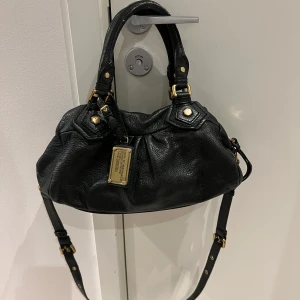 Marc Jacobs väska  - Snygg svart handväska från Marc Jacobs i skinn med gulddetaljer. Väskan har en praktisk dragkedja och ett mönstrat innerfoder. Perfekt för att ge en stilren touch till din outfit. Perfekt att önskar sig till julklapp eller bara  present för dig själv🤩💞 Kan gärna skicka fler bilder🙃