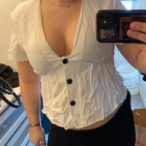 Vit blus med knappar - Säljer en söt vit blus med korta ärmar och stora svarta knappar framtill. Blusen har en v-ringad design 🤍
