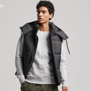 Svart dunväst från Superdry - Snygg svart dunväst från Superdry med broderad logga på bröstet. Västen har en quiltad design och dragkedja framtill. Perfekt för kyligare dagar. aldrig använd !pris går och diskutera 