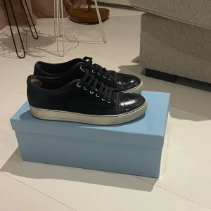 Svarta sneakers från Lanvin - Snygga svarta sneakers från Lanvin med vit sula och klassisk snörning. Perfekta för en stilren look. Skorna kommer i ej originalkartong. Priset kan diskuteras och kan sänkas lite. Effekt i hälen i en av skorna. Priset är ej hugget i sten och kan diskuteras‼️