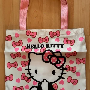 Stor Hello Kitty totebag! - Söt, stor totebag med Hello Kitty-motiv i slitstark canvas. Väskan har rosa handtag och en praktisk dragkedja för säker förvaring. Mått: 40 x 35 cm. Ny och oanvänd. Perfekt för alla Hello Kitty-fans! 