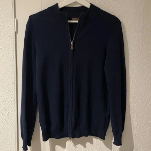 Mörkblå kofta från Stenströms - Snygg och stilren mörkblå kofta från Stenströms med dragkedja framtill. Perfekt för kyligare dagar med sin ribbade krage och långa ärmar. Ett klassiskt plagg som passar till många tillfällen.