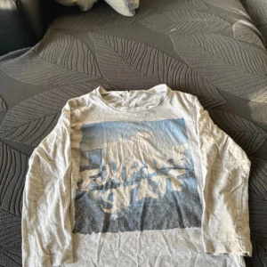 Vit långärmad t-shirt med tryck - Vit långärmad t-shirt med ett stort tryck i blått och grått på framsidan. Perfekt för en avslappnad stil.