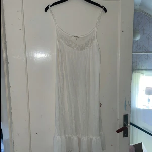 Vit klänning från RoseBud - Säljer en elegant vit klänning från RoseBud i storlek L. Klänningen har en vacker spetsdetalj vid halsen och är ärmlös med en lös passform. Perfekt för sommarens fester eller en avslappnad dag på stranden. 🏖️