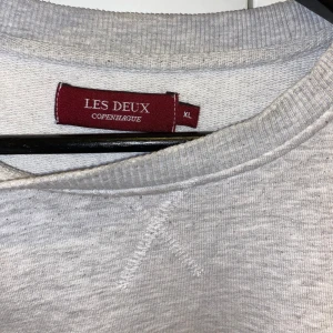 Grå sweatshirt från Les Deux - En stilren grå herr sweatshirt från Les Deux med texten 'IVY LEAGUE' tryckt i svart sammet typ på framsidan. Storlek XL men mer som M/L. Perfekt för en avslappnad vardag nu till hösten!! 😍