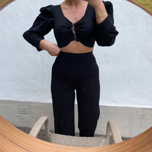 Svart croppad topp från Boohoo - Säljer en snygg svart croppad topp från Boohoo. Den har långa ärmar och knappar framtill som ger en stilren look. Aldrig använd och liten i storleken. Perfekt för en utekväll eller fest!