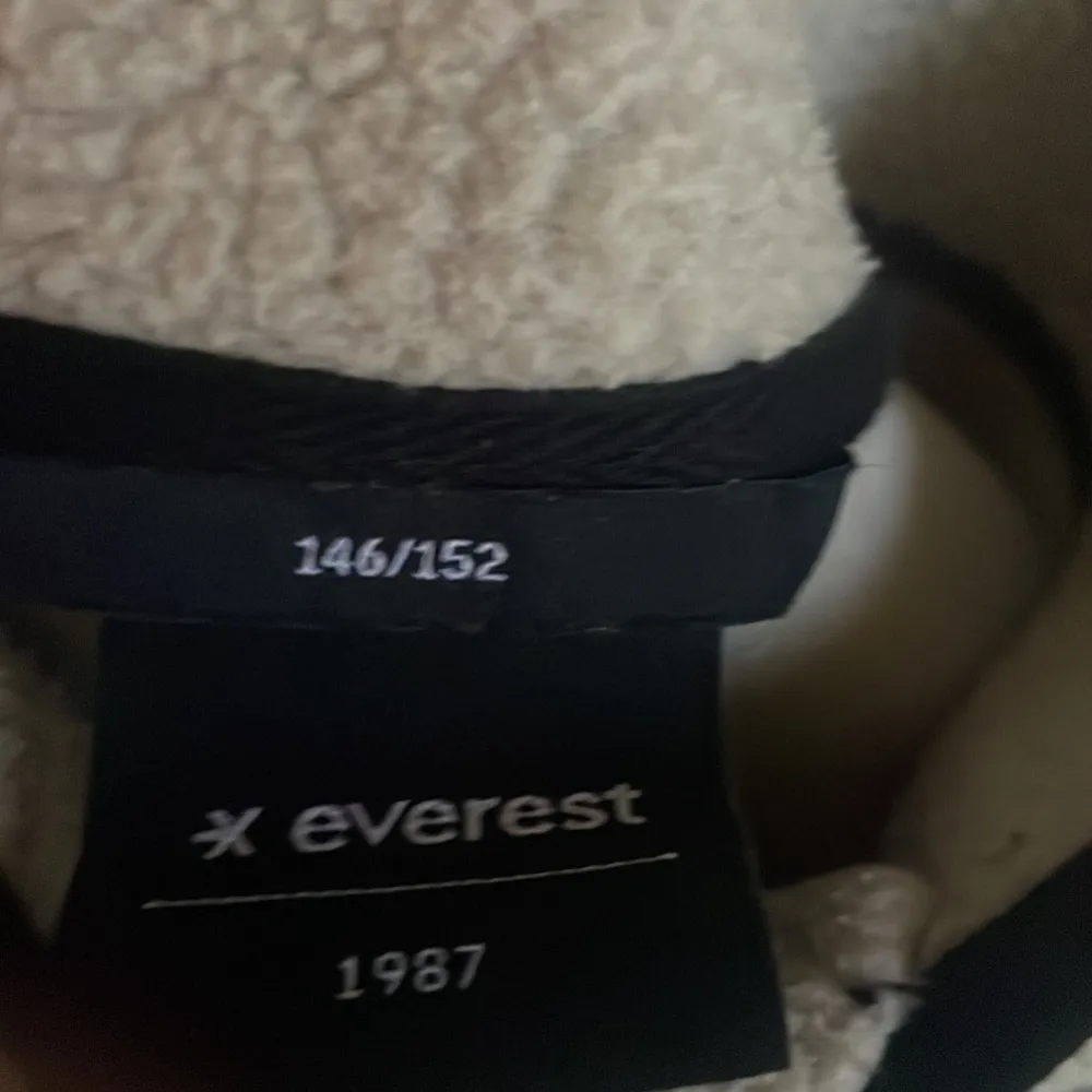 Säljer en supermysig beige fleecejacka från Everest. Den har en dragkedja framtill och svarta detaljer som ger en snygg kontrast. Perfekt för kyliga dagar och passar både till vardags och utomhusaktiviteter. Jackan har en praktisk bröstficka och två sidofickor.. Takit.