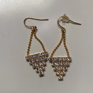 Guldörhängen med glittriga stenar - Säljer ett par superfina guldörhängen med glittriga stenar i en triangulär design. De hänger snyggt och är perfekta för att lysa upp vilken outfit som helst. Passar perfekt till fest eller en utekväll! ✨