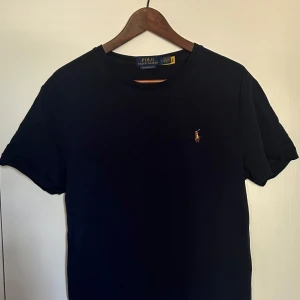 Mörkblå t-shirt från Polo Ralph Lauren - Säljer en snygg mörkblå t-shirt från Polo Ralph Lauren i storlek M. Den har en klassisk design med korta ärmar och en liten broderad logga på bröstet. Perfekt för en stilren och avslappnad look!