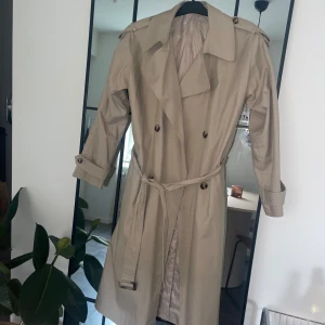 trenchcoat  - Snygg trenchcoat till höst/vår  har en liten fläck (se bild 3) men inget märkbart i verkligheten och kan säkert gå bort med lite jobb