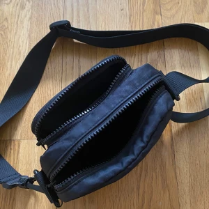 Väska - Super trendig väska från Monki med flera fickor, bandet går att justera i längd🖤