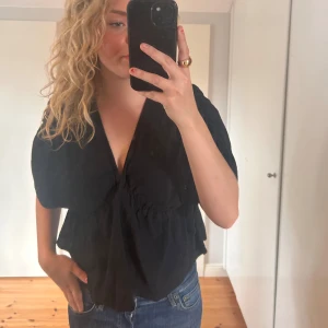 Svart blus från ASOS DESIGN - Säljer en snygg svart blus från ASOS DESIGN. Den har en v-ringad design med knytning i midjan. Perfekt för både vardag och fest!🖤🪩