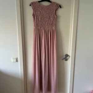 Rosa långklänning från Bubbleroom - Säljer en superfin rosa långklänning från Bubbleroom. Klänningen har ett vackert spetsmönster på överdelen och är ärmlös. Den har en elegant öppen rygg och är perfekt för festliga tillfällen. Materialet känns lyxigt och faller snyggt.