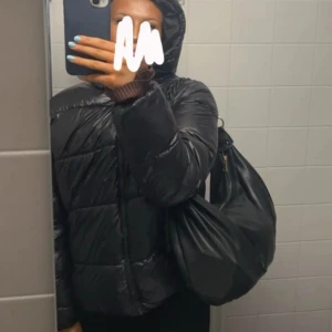 Svart pufferjacka - Säljer en svart pufferjacka som är perfekt för kyliga dagar. Jackan har en glansig yta och är långärmad med en dragkedja framtill. Den är både stilren och praktisk, idealisk för höst och vinter. Den är endast använd 1 gång så inprincip som ny!