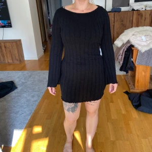 Svart stickad klänning med öppen rygg - Säljer en superfin svart stickad klänning med långärmad design och en snygg öppen rygg. Klänningen är tight och perfekt för både vardag och fest. Den har en ribbad struktur som ger en extra touch av stil. Passar perfekt till höst och vinter!