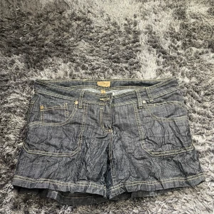 Jeansshorts från Broadway Fashion - Säljer ett par snygga jeansshorts från Broadway Fashion. De är i en klassisk blå jeansfärg med coola kontrastsömmar. Shortsen har en normal passform och är perfekta för sommaren. De har praktiska fickor både fram och bak, vilket är super för att ha med sig småsaker. Perfekta för en avslappnad dag ute eller en sommarfest!