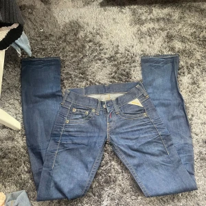 Blå jeans från Replay - Säljer ett par snygga blå jeans från Replay. De har en klassisk femficksdesign med knappar och dragkedja fram. Jeansen är i en normal passform och är perfekta för vardagsbruk. Märket Replay är känt för sin kvalitet och stil. Passar perfekt till både vardag och fest!