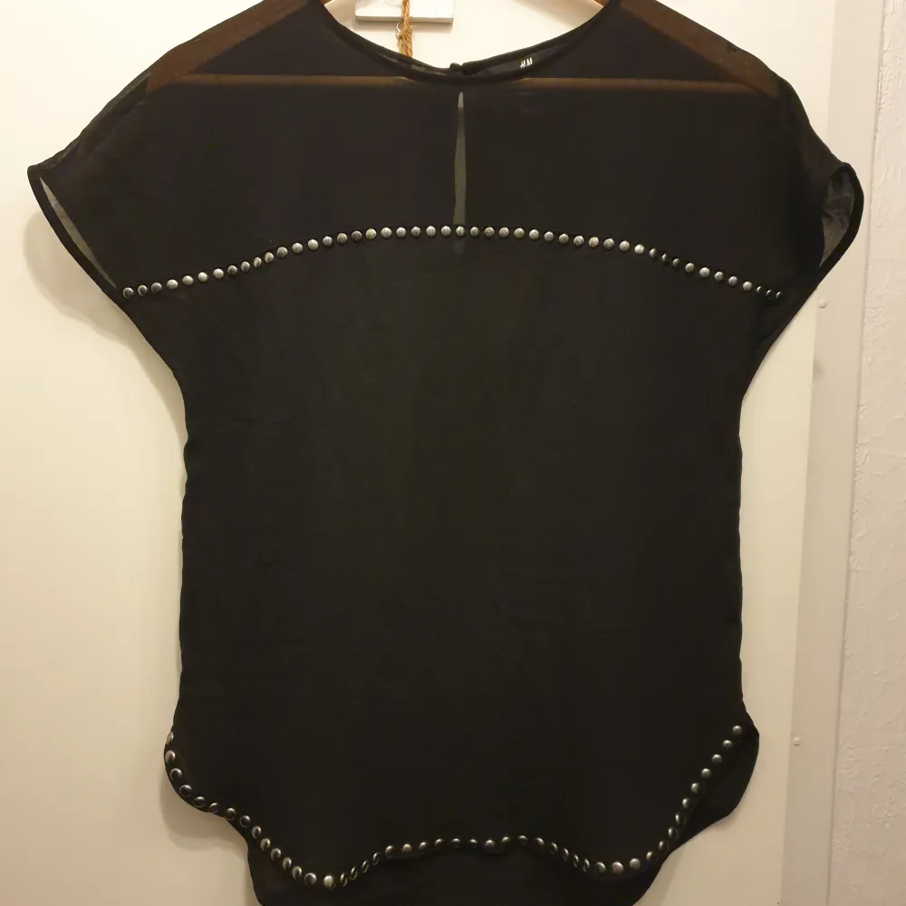 Säljer en Ny, snygg svart topp från H&M i storlek S. Toppen har korta ärmar och är dekorerad med coola nitar längs ärmarna och nederkanten. Perfekt för en kväll ute eller en avslappnad dag med stil.. Yläosat.