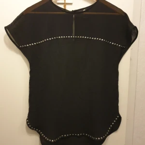 Svart topp med nitar från H&M - Säljer en Ny, snygg svart topp från H&M i storlek S. Toppen har korta ärmar och är dekorerad med coola nitar längs ärmarna och nederkanten. Perfekt för en kväll ute eller en avslappnad dag med stil.