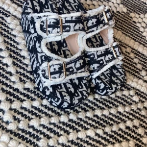 Svartvita mönstrade ballerinaskor - Säljer ett par unika svartvita ballerinaskor med ett coolt mönster. Skorna har två justerbara remmar med guldfärgade spännen och en mjuk kant i vitt. Perfekta för att ge din outfit en extra touch!