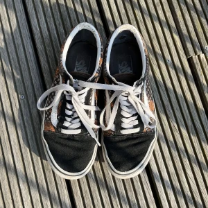 Vans - Låga vans i stl 38.5, låga svarta med små vita blommor och tigrar på sidan.