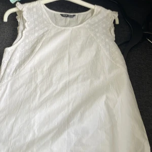 Vit ärmlös topp från Shein - Säljer en stilren vit ärmlös topp från Shein. Toppen har fina spetsdetaljer vid axlarna och en rund halsringning. Perfekt för varma dagar eller som ett lager under en jacka.