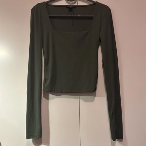 Mörkgrön långärmad topp från Amisu - Snygg mörkgrön långärmad topp från Amisu med en fyrkantig halsringning. Perfekt för en stilren look. Tillverkad i ett mjukt och stretchigt material för extra komfort.