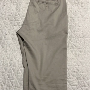 Beige chinos från East West - Snygga beige chinos från East West med skin fit passform. Byxorna har en klassisk design med knappar och fickor både fram och bak. Perfekta för en stilren look.