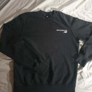 New Balance sweatshirt - Säljer en stilren svart sweatshirt från New Balance med deras logga tryckt på bröstet i storlek XS. Tröjan har långa ärmar och en klassisk rund halsringning. Loggan på bröstet är något slitet men inget man ser om man inte kollar på väldigt nära håll. Anledning till att jag säljer den är att den är för liten.