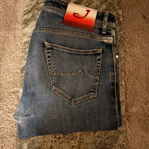 Blå jeans från Jacob Cohen - Snygga blå jeans från Jacob Cohen med klassisk femficksdesign och kontrastsömmar. Perfekta för en stilren look. Nypris 6000kr Fins en defekt som är ett hål men är lagat