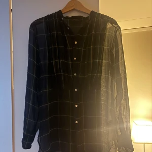 Svart och grön rutig blus från Polo Ralph Lauren - Snygg svart och grön rutig blus från Polo Ralph Lauren med knappar framtill. Blusen har långa ärmar och en klassisk krage, perfekt för en stilren look.