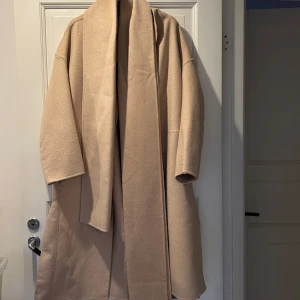 Beige wool blend kappa från H&M med scarf  - Säljer en stilren beige kappa från H&M i ullblandning och med tillhörande scarf. Den har en elegant och enkel design med långa ärmar och en öppen front. Perfekt för kyligare dagar.