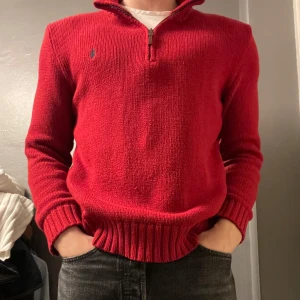 Röd stickad tröja från Ralph Lauren - Snygg röd stickad tröja från Ralph Lauren med dragkedja vid halsen. Tröjan har långa ärmar och ribbade muddar vid ärmslut och nederkant. Perfekt för kyligare dagar!