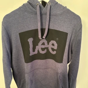 Blå hoodie från Lee - Säljer en snygg blå hoodie från Lee med deras ikoniska logga i svart på framsidan. Tröjan har en klassisk design med huva och dragsko samt långa ärmar. Perfekt för en avslappnad stil.nypris 700kr