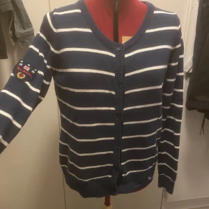 Blå och vit randig kofta från Bondelid - Snygg blå och vit randig kofta från Bondelid med broderad detalj på ärmen. Perfekt för en avslappnad stil med knappar framtill och ribbade muddar.