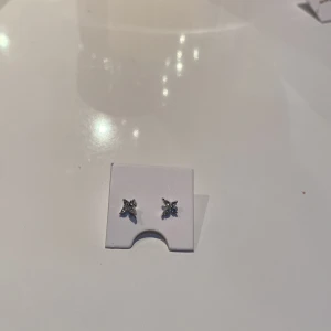 Silvriga örhängen med stenar - Säljer ett par eleganta silvriga örhängen med glittrande stenar. Perfekta för att ge en touch av glamour till din stil. De är små och diskreta, vilket gör dem lätta att bära till olika tillfällen.