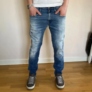 Replay jeans med slitningar  - Snygga blå jeans med slitningar och en modern tvätt. De har en slim passform och är perfekta för en avslappnad stil. Jeansen har klassisk femficksdesign och knappar i gylfen. Modellen heter anbass och är köpt på nk för ungefär 1800. 