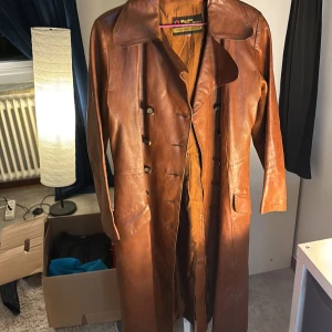 Brun skinnrock från Torsten Albertssons - Säljer en snygg brun skinnrock från Torsten Albertssons. Rocken har en klassisk design med knappar framtill och en stilren krage. Perfekt för höst och vår, med ett randigt foder som ger extra komfort.