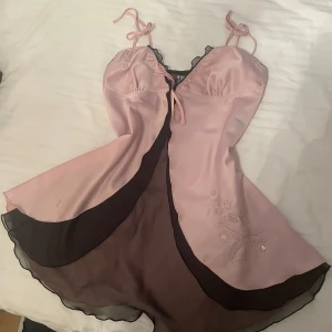 Rosa nattlinne med broderade detaljer - Charmigt rosa nattlinne med broderade blommor och fjärilar. Har tunna axelband med knytning och en subtil svart kant. Storlek M. Har inte något märke