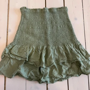 Grön kjol från Mango - Snygg grön kjol från Mango med smockdetaljer och volangkant. 