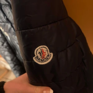 Svart quiltad jacka från Moncler - Snygg svart quiltad jacka från Moncler med dragkedja framtill. Perfekt för kyligare dagar med sin stilrena design och bekväma passform.