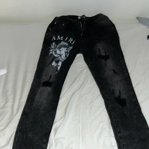 Svarta jeans från Amiri - Snygga svarta jeans från Amiri med slitna detaljer och ett coolt tryck av en ängel på framsidan. Tillverkade i bomull med lite stretch för extra komfort. Perfekta för en trendig look.
