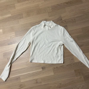 Vit ribbad polotröja - Säljer en stilren vit ribbad polotröja med långa ärmar. Perfekt för lager-på-lager under kyligare dagar. Enkel och tidlös design som passar till det mesta. Hör av dig vid intresse!