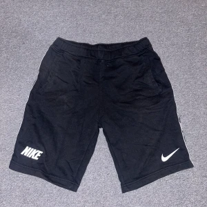 Svarta shorts från Nike - Snygga svarta shorts från Nike med logga på benet. Perfekta för träning eller en avslappnad dag. Elastisk midja för extra komfort.