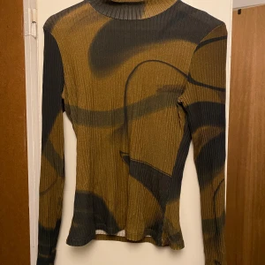  Paloma Wool - Säljer en unik ribbad tröja från Paloma Wool i gröna och bruna toner med abstrakt mönster. Tröjan har långa ärmar och är tillverkad av ekologisk bomull med en liten del elastan. Står storlek L, men passar en M. 